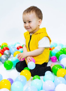 Balonların üzerinde oturan genç bir çocuk. Etrafı Renkli Yüzen Nesnelerle çevrili Neşeli Bir Genç