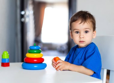 Bir dizi renkli oyuncakla çevrili Oynak bir çocuk. Bir yığın oyuncakla masada oturan küçük bir çocuk.