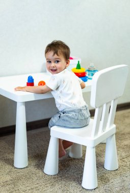 Beyaz bir masada oyuncaklarla oturan küçük bir çocuk. Yaratıcı bir oyun oynayan Oyuncu Küçük Çocuk
