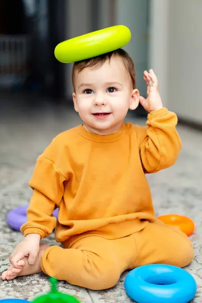 Alışılmadık bir şapkası olan oyuncu bir çocuk. Kafasında frizbiyle yerde oturan küçük bir çocuk.