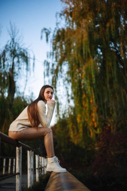 Ağacın önündeki korkulukta oturan bir kadın. Demiryolunda oturan kadın, Doğa 'nın Huzuru' nun tadını çıkarıyor.