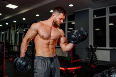 İyi donanımlı bir spor salonunda kaslı, güçlü ve formda bir adam. Spor salonunda iki dubanı tutan üstsüz bir adam.