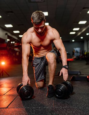 Bir adam spor salonunda dambıllarla egzersiz yapıyor. Modern Fitness Stüdyosunda Ağırlıklarla Kaslarını Heykel Yapan Bir Adam