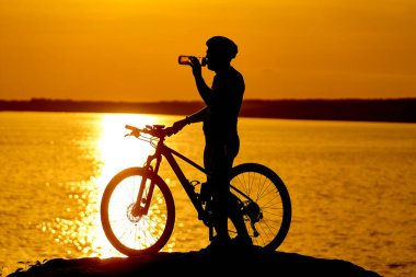 Kayanın üstünde bisikletin yanında duran bir adam. Doğanın güzelliğiyle çevrili bir adam.