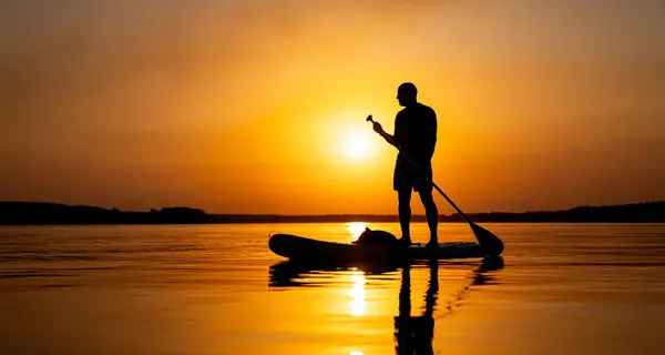 A man standing on a paddle board in the water. A Serene Moment: Man Standing on Paddle Board in Calm Waters