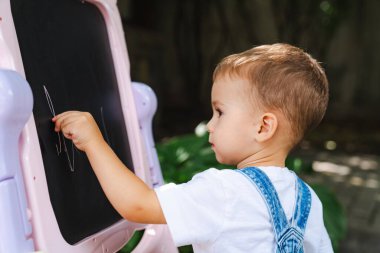 Tahtaya yazı yazan küçük bir çocuk. Meraklı Küçük Bilgin Yaratıcılığını Tahtaya Salıyor