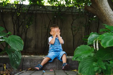 Bir bankta oturan küçük bir çocuk yüzünü örtüyor. Gölgelerde Solace Arayan Meraklı Bir Çocuk