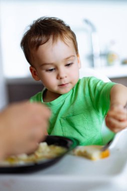 Masada oturan küçük bir çocuk yemek yiyor. Lezzetli yemeğin tadını çıkaran Meraklı Küçük Çocuk