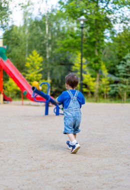 Oyun parkına Neşeli Yolculuk. Küçük bir çocuk parkta kayağa doğru koşuyor.