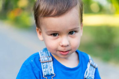Mavi gömlek ve pantolon askısı giyen genç bir çocuk. Mavi tişörtlü ve askılı meraklı bir genç.