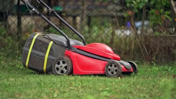 庭の背景で働く 庭師は赤い電力で草を刈る — ストック動画