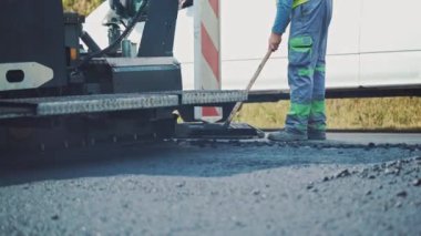 Yol inşaatında çalışan bir işçi. İşçilerin ve asfaltlama makinelerinin görüntüsünü kapat.