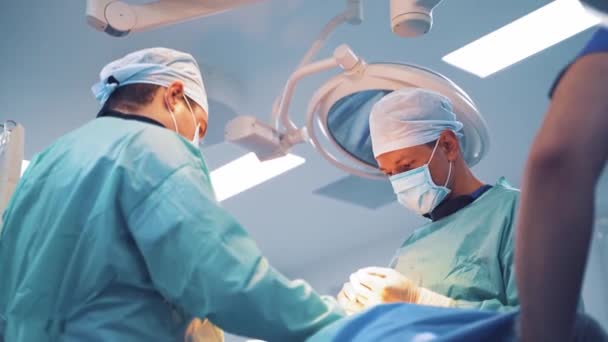 手術室で働いている外科医のグループ 熟練した外科医は手術中にメスとクランプで作業します — ストック動画