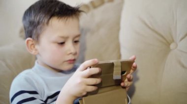Evde telefon kullanan bir çocuk. Güzel küçük çocuk kanepede dinleniyor ve akıllı telefona bakıyor.