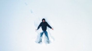 Yetişkin adam kardan melekler yapıyor. Karda yatıp kar meleği figürü yaratan mutlu adamın yüksek açılı görüntüsü