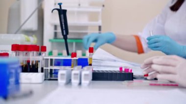 Laboratuvar teknisyeni kan tüpü örneğini incelemek için tutuyor. Tıbbi teknisyen hastane laboratuarındaki test tüpüne kan bırakıyor.