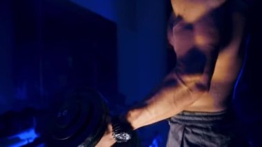 Dambılı atletik genç adam. Spor salonundaki kaslı adam pazularda halterlerle egzersiz yapıyor.