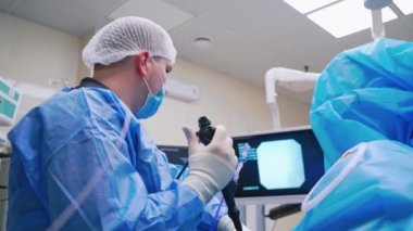 Laparoskopik ekipman kullanan bir doktor. Doktorun arka görüntüsü hastanede ameliyat öncesi monitörlere bakıyor