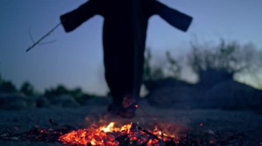Ateşin yanında siyah cüppeli korkunç bir ölüm. Yerde ateş közleri ve gizemli figür tahta bir sopayla şamanizm yapıyor. Cadılar Bayramı.