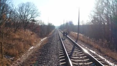 Tırabzanda yürüyen iki çocuğun arka görüntüsü. Çocuklar güneşli bir kış gününde demiryolu boyunca gidiyorlar. Tehlike kavramı.