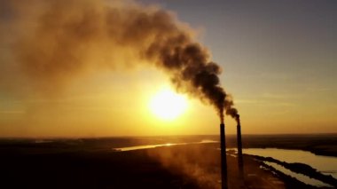 Gün batımında doğada kirli emisyonlar. Sarı güneş batan arka plandaki endüstriyel borulardan yoğun duman geliyor. Ekolojik felaket.