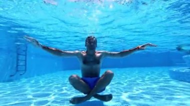 Yoga pozunda suyun altında oturan adam. Yüzme havuzunda egzersiz yapan sağlıklı bir adamın sualtı görüntüsü. Su altı sporu.