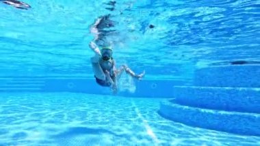 Genç çocuk yüzme havuzunda eğleniyor. Maskeli çocuk havuzda suyun altında eğleniyor. Mutlu yaz tatilleri..
