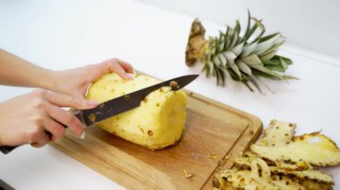 Ahşap bir tahtanın üzerinde taze soyulmuş ananas. Kadının elleri masada keskin bir bıçak ve ananas tutuyor..
