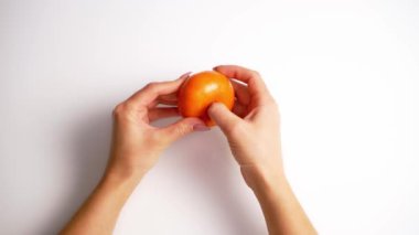 Küçük turuncu narenciye ellerinde. Beyaz arka planda mandalina temizleyen kadın elleri. Üst görünüm.