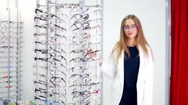 Optik mağazasında güzel bir kadın. Moda giysileri içinde gülümseyen genç bayan dükkandan modern gözlükleri seçiyor..