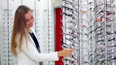 Optik dükkanındaki kadın alıcının yan görüntüsü. Genç ve güzel bir kadın yeni gözlük seçiyor. Sağlık hizmetleri kavramı.