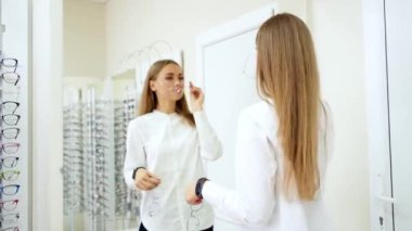 Optik mağazasındaki kız. Yeni gözlüklü güzel kadın aynadaki yansımasına bakıyor. Gözlük seçimi..