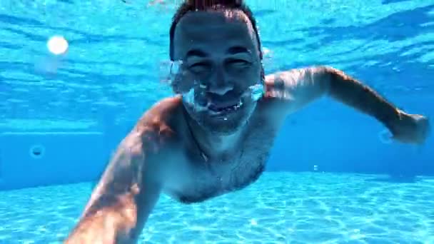 男人在水下游泳健康的男人在游泳池里潜水 看着镜头 快乐的男人在池子里签名 — 图库视频影像