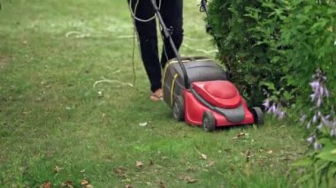 Bahçesinde çim biçen kadın elektrikli çim biçme makinesiyle.