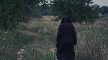 Sahadaki cadının arkadan görünüşü. Kara ölüm, doğanın arka planında yavaş yavaş kaybolur..