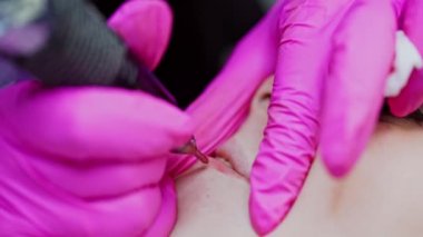 Mikroplama prosedürü. Genç kız dudaklarına kalıcı makyaj dövmesi yapıyorum. Elleri koruyucu eldivenlerle dudaklarında dövme yapan bir kozmetik uzmanı. Yakın plan..