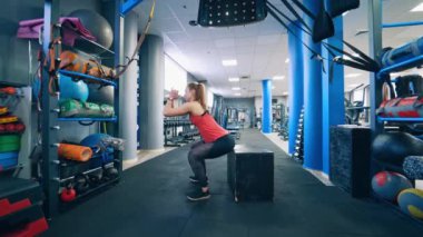 Spor kulübündeki bir kızın yan görüntüsü. Genç bir kadın modern fitness merkezinde tahta kutunun yanında çömeliyor. Sağlıklı yaşam tarzı.