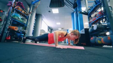 Atletik kadın antrenmanın bir parçası olarak şınav çekiyor. Spor kıyafetli bir kız spor salonundaki paspasın üstünde şınav çekiyor..
