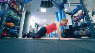 Paspasın üzerinde şınav çeken genç bir bayan. Spor salonunda yerde antrenman yapan bir kızın yan görüntüsü. Spor giyim sektöründe spor yapan aktif bir kadın..