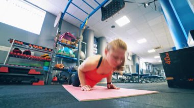 Paspasın üzerinde egzersiz yapan güzel bir kız. Spor kıyafetli genç bir kadın modern fitness merkezinde şınav çekiyor..