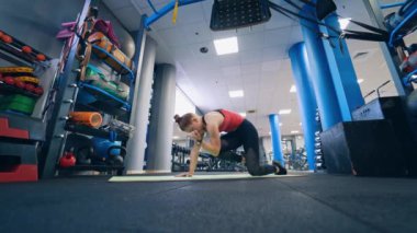 Spor salonunda spor giyim eğitimi alan genç bir kız. Modern fitness merkezinde paspasın üzerinde egzersiz yapan aktif bir kadın. Sağlıklı yaşam tarzı.