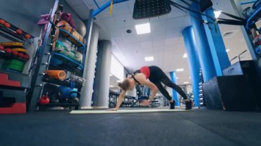 Spor salonunda spor antrenmanı. Spor takım elbiseli genç bir kadın modern fitness kulübünde paspasın üzerinde egzersiz yapıyor..
