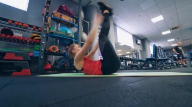 Formda kız spor salonunda paspas üzerinde egzersiz yapıyor. Genç bir kadın modern fitness merkezinde ince vücudunu esnetiyor ve büküyor..