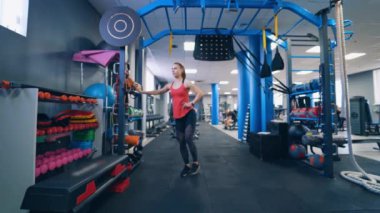 Spor salonunda egzersiz yapan genç bir kadın. Modern fitness kulübünün arka planında bacaklarını çalıştıran sportif bir kadın..