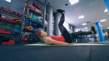 Spor salonunda spor yapan genç bir kadın. Sportif kız paspasa uzanıp bacaklarını kaldırıyor spor salonunun arka planında..