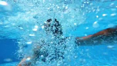 Havuzda bir adam var. Yüzme havuzunun berrak mavi sularında yüzen ve kameraya bakan sağlıklı bir adam. Yaz tatili.