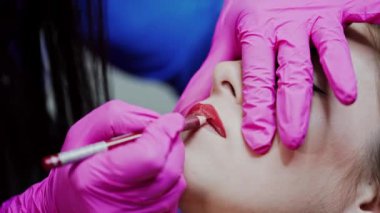 Güzellik salonunda daimi dudak makyajı. Kozmetik uzmanı genç bir kızın yüzüne kırmızı bir kalemle dudak çizer. Yakın plan..