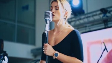 Sarışın kadın mikrofona şarkı söylüyor. Sahnede durup şarkı söyleyen çekici bir şarkıcı. Müzik eğlencesi.