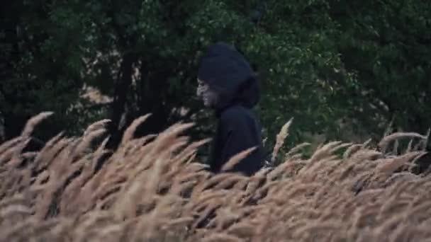 战场上黑影的侧视图 身穿黑色服装 头罩在绿树成荫的背景上行走的鬼魂 女巫可怕的脸万圣节时间 — 图库视频影像