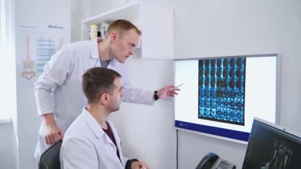 医生在诊所检查病人的诊断 男性专家研究脊柱X光 并在现代内阁中与一位女性交谈 — 图库视频影像